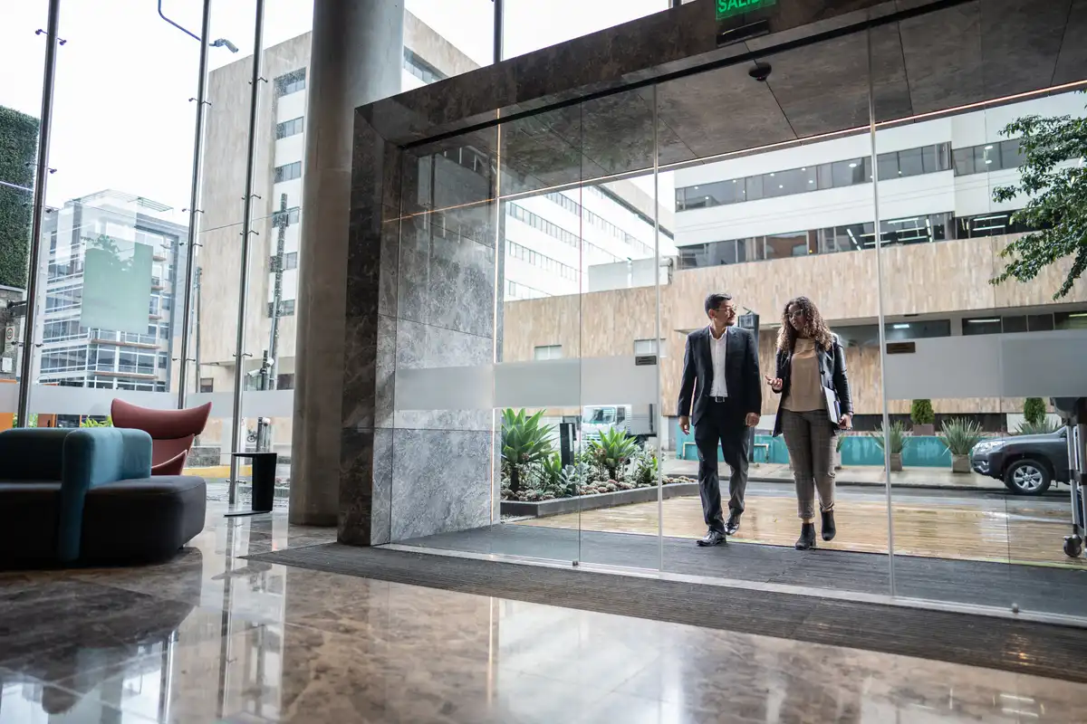 Dos personas caminando por el hall de vidrio de un edificio de oficinas