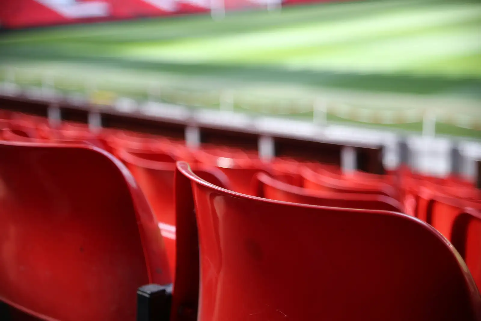 Butacas rojas de una tribuna con el campo deportivo desenfocado al fondo
