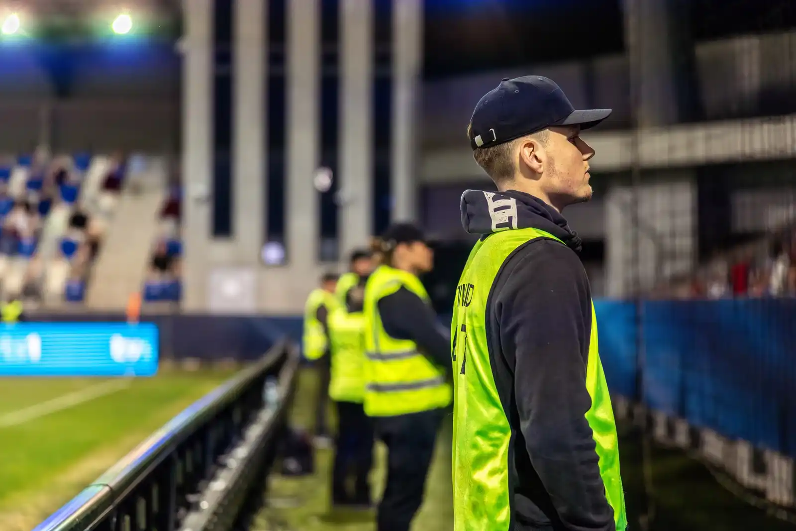 Personal de seguridad con pechera de espaldas frente al público de un estadio